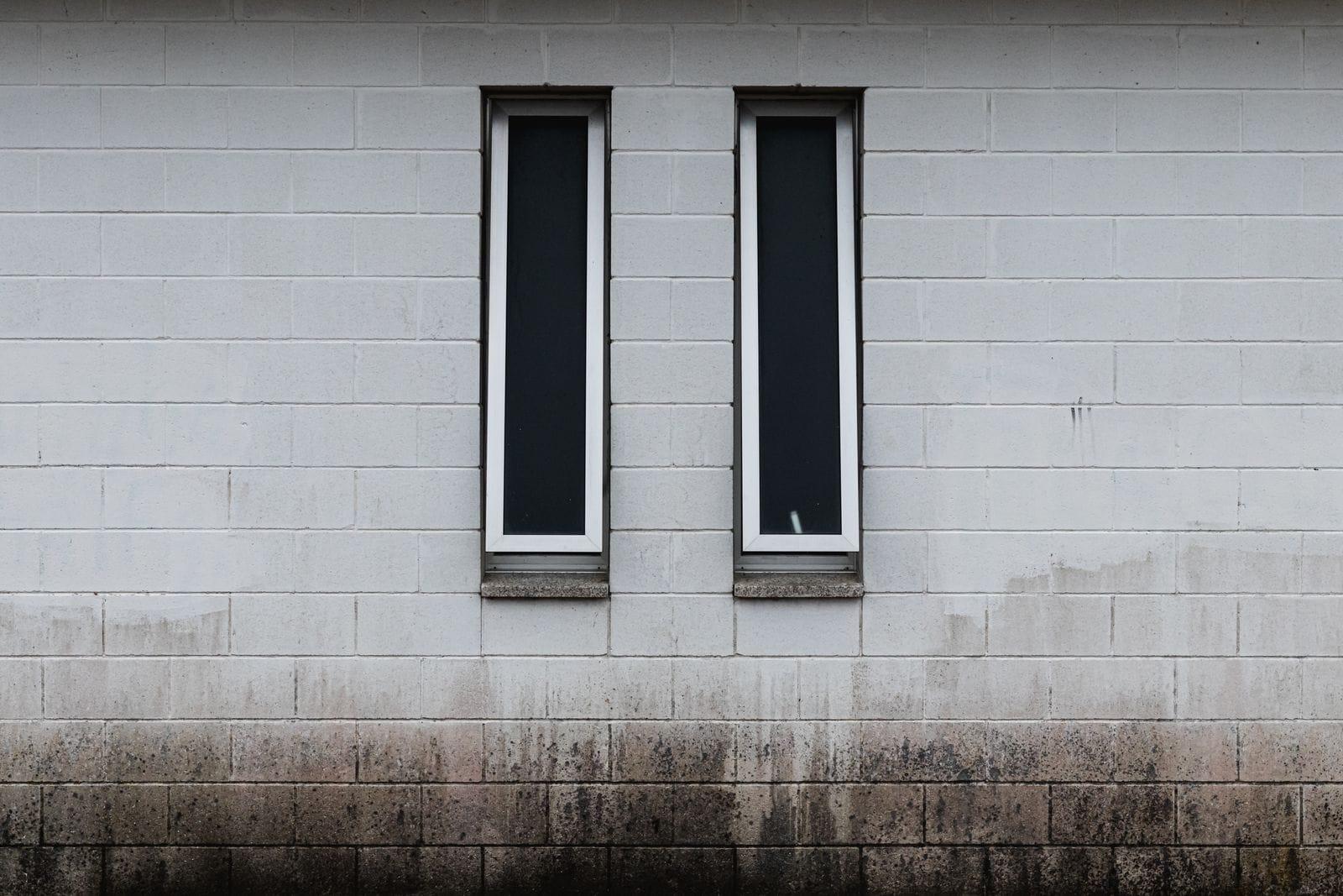 Concrete block wall with two narrow windows and dark staining along its base