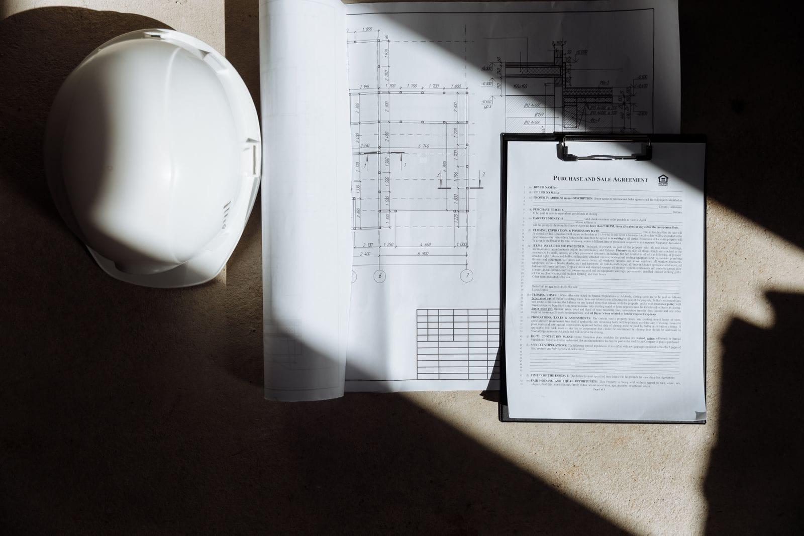 Hard hat, clipboard with paperwork, and building plans on a table