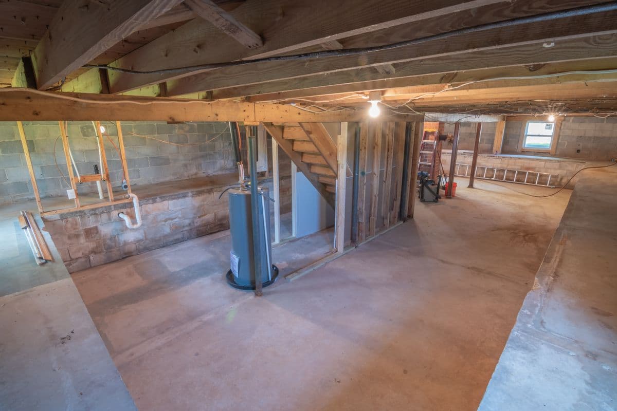 Unfinished basement with exposed joists and a concrete floor, before waterproofing